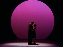 两个演员在舞台上拥抱在一起，舞台上有一个巨大的粉色聚光灯照在他们身上